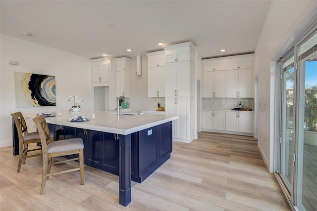 kitchen featuring white cabinetry, sink, a breakfast bar area, a large island with sink, and light wood-type flooring