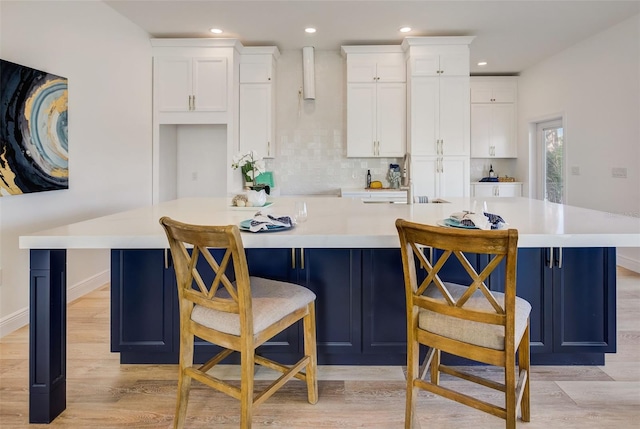 kitchen with a breakfast bar area, white cabinetry, light wood-type flooring, a large island, and backsplash