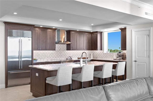 kitchen with wall chimney range hood, an island with sink, a kitchen bar, and high quality appliances