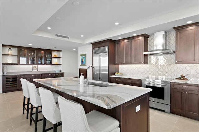 kitchen featuring an island with sink, wall chimney exhaust hood, a breakfast bar area, and stainless steel appliances