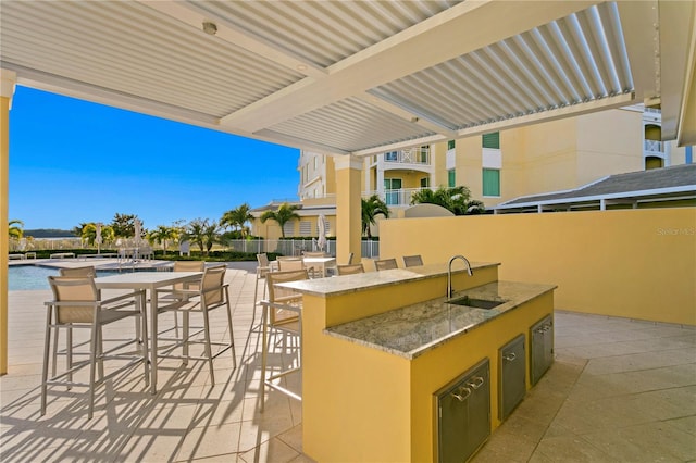 view of patio featuring a wet bar, a balcony, an outdoor kitchen, and a community pool