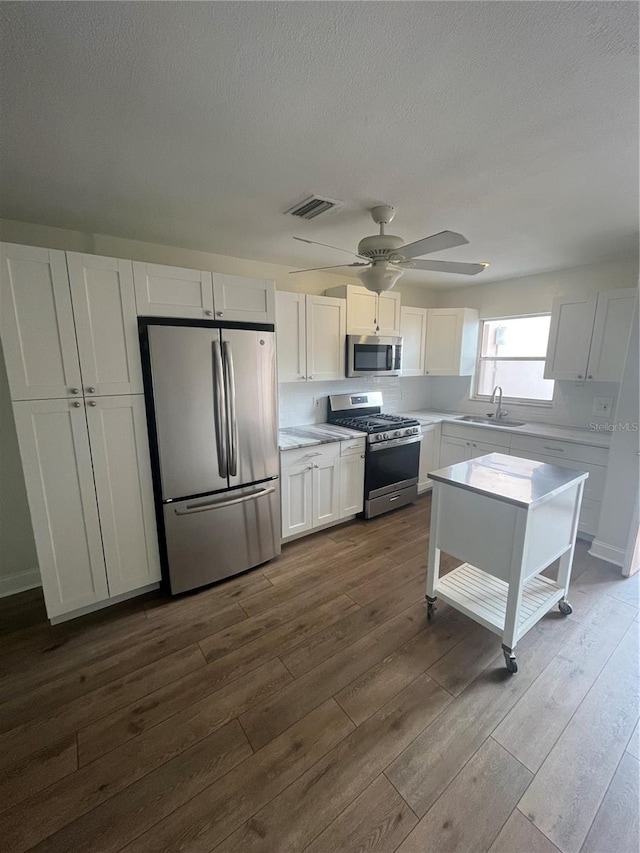 kitchen with appliances with stainless steel finishes, white cabinetry, and dark wood-type flooring