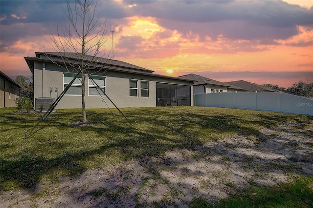 back house at dusk with central AC unit and a lawn