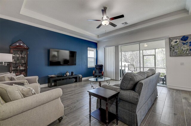 living room featuring ornamental molding, wood-type flooring, ceiling fan, and a tray ceiling