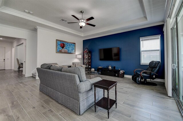 living room featuring light hardwood / wood-style flooring, ornamental molding, a raised ceiling, ceiling fan, and a textured ceiling