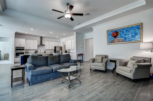 living room featuring ceiling fan, a textured ceiling, light hardwood / wood-style floors, a tray ceiling, and crown molding