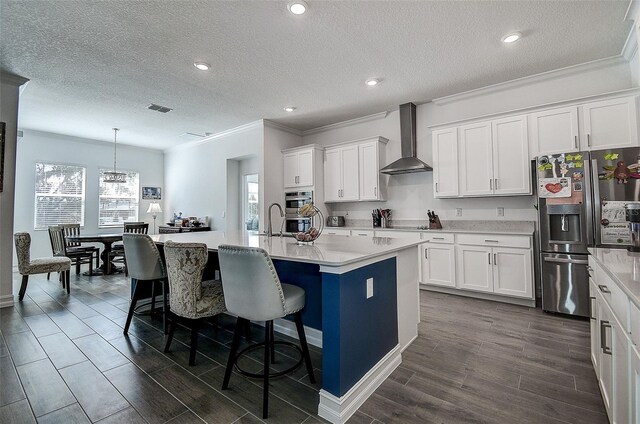 kitchen featuring a healthy amount of sunlight, wall chimney range hood, decorative light fixtures, and an island with sink