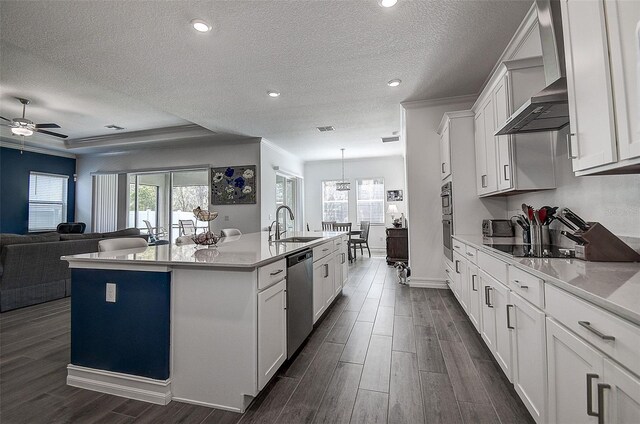 kitchen featuring ceiling fan with notable chandelier, dark hardwood / wood-style floors, an island with sink, wall chimney exhaust hood, and white cabinets