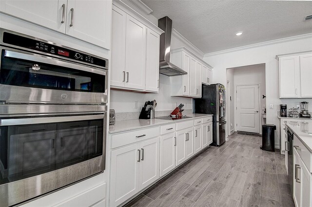 kitchen featuring wall chimney exhaust hood, white cabinets, light hardwood / wood-style flooring, ornamental molding, and stainless steel appliances