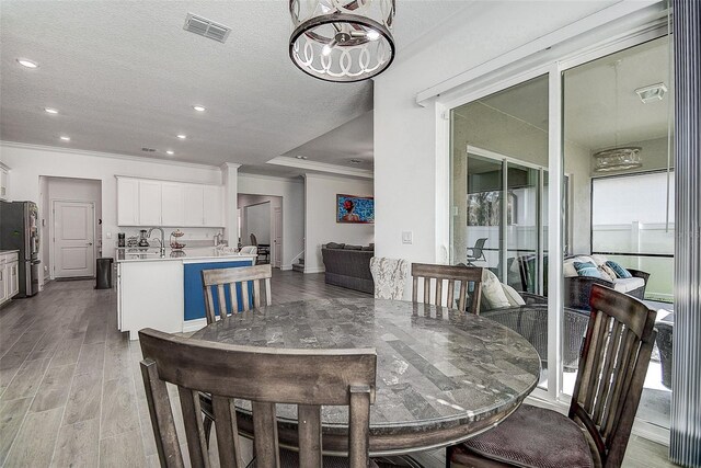 dining area with ornamental molding, a notable chandelier, light wood-type flooring, and a textured ceiling