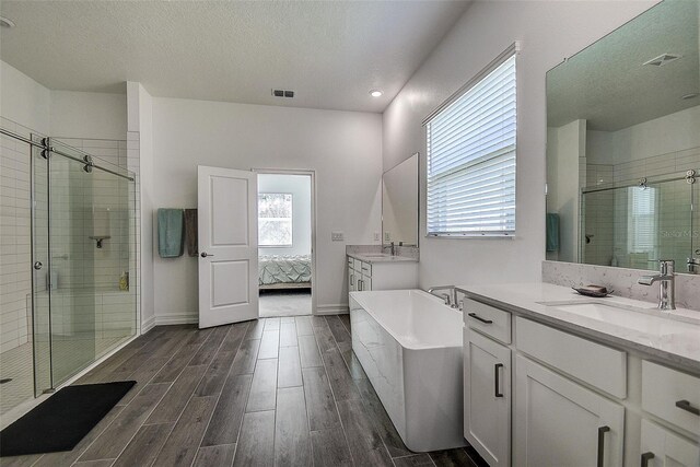 bathroom featuring a textured ceiling, hardwood / wood-style floors, vanity with extensive cabinet space, and separate shower and tub