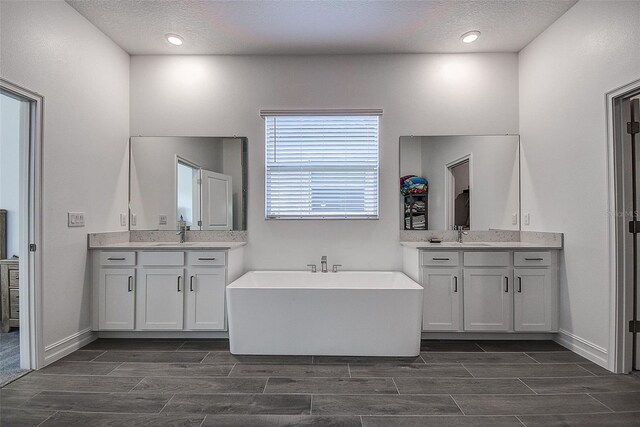 bathroom with double vanity, a textured ceiling, and a bath