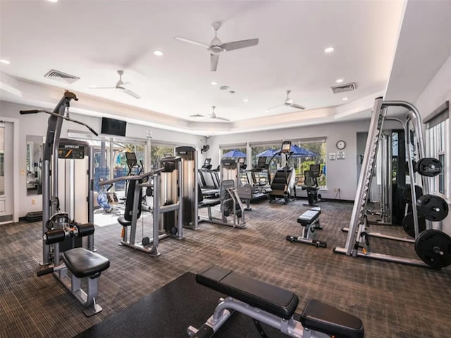 exercise room featuring ceiling fan, dark carpet, and a tray ceiling