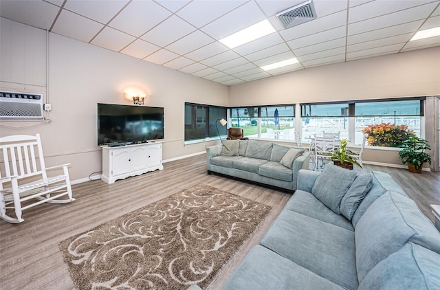 living room featuring wood finished floors, baseboards, visible vents, a wall mounted AC, and a drop ceiling