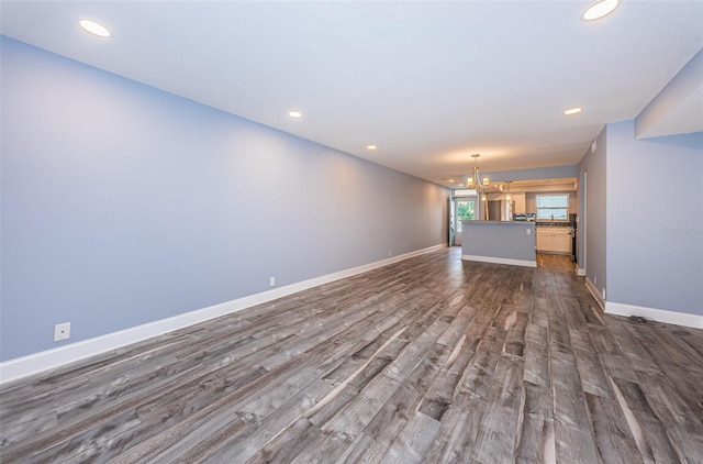 unfurnished living room with recessed lighting, baseboards, a notable chandelier, and wood finished floors