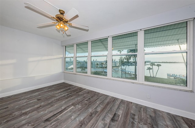 empty room with baseboards, dark wood-type flooring, ceiling fan, and a water view