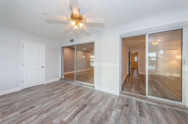 unfurnished bedroom featuring visible vents, baseboards, wood finished floors, a closet, and a ceiling fan