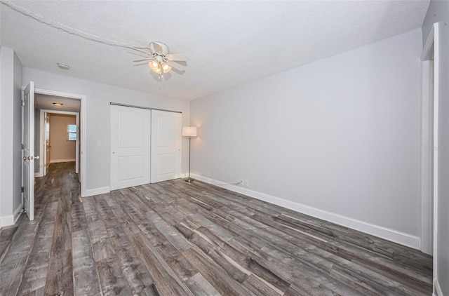 unfurnished bedroom with dark wood-style floors, a textured ceiling, a closet, and baseboards