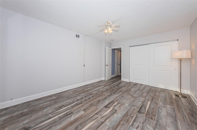 unfurnished bedroom featuring visible vents, baseboards, wood finished floors, a closet, and a textured ceiling