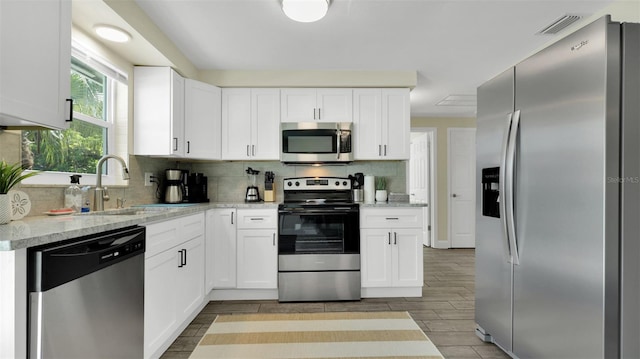 kitchen with stainless steel appliances, light stone countertops, tasteful backsplash, white cabinets, and sink