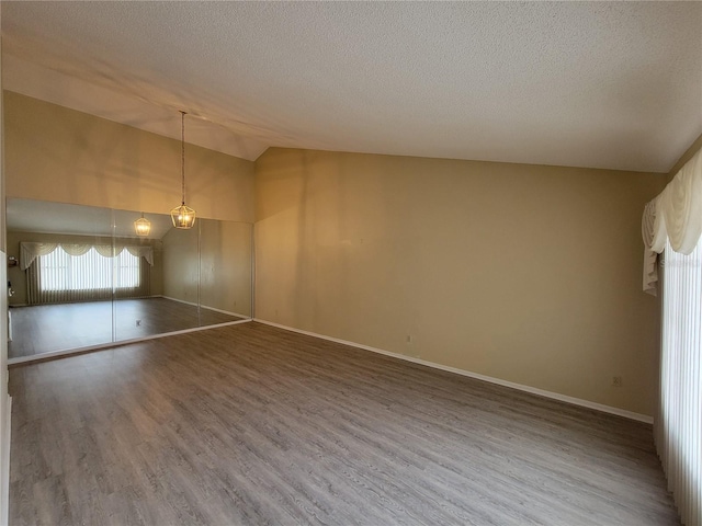 empty room featuring hardwood / wood-style floors, a textured ceiling, a chandelier, and vaulted ceiling