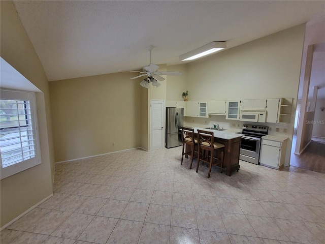 kitchen with ceiling fan, light tile floors, stainless steel appliances, high vaulted ceiling, and white cabinetry