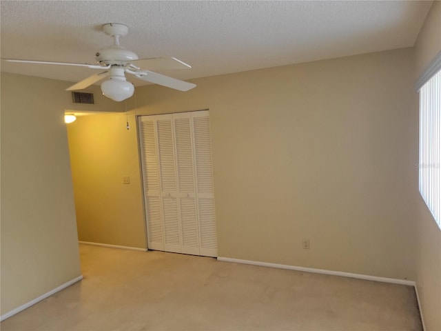 unfurnished bedroom with light carpet, a closet, ceiling fan, and a textured ceiling