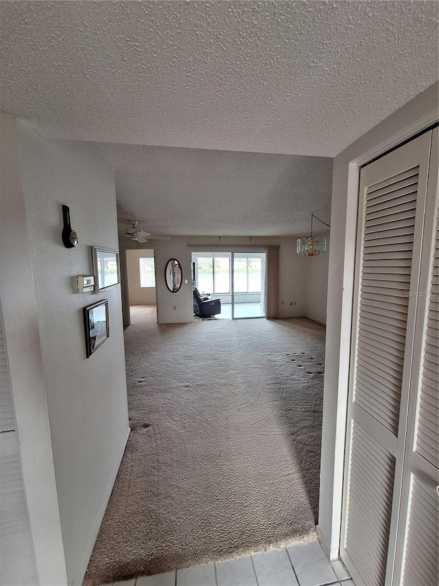 unfurnished living room with ceiling fan with notable chandelier, a textured ceiling, and light carpet