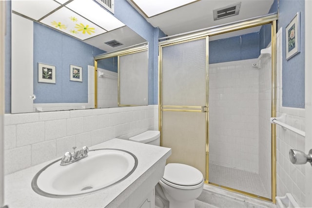 bathroom with vanity, toilet, a shower with shower door, and tile walls