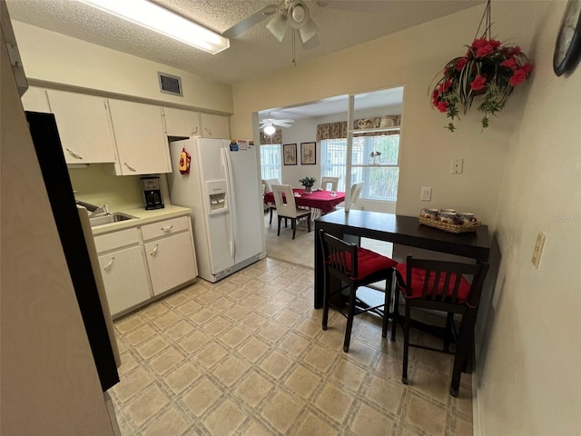 kitchen featuring ceiling fan, sink, a textured ceiling, white cabinetry, and white refrigerator with ice dispenser