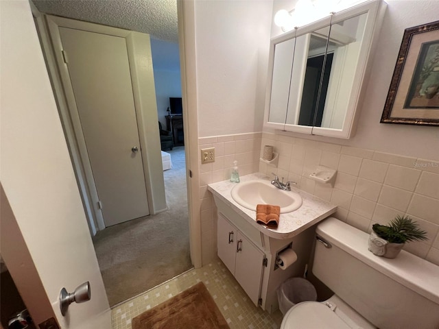 bathroom featuring vanity, tile walls, toilet, and a textured ceiling