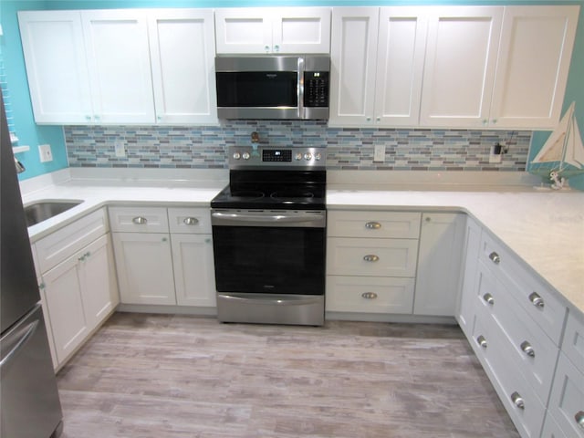 kitchen featuring appliances with stainless steel finishes, light hardwood / wood-style floors, white cabinetry, and backsplash