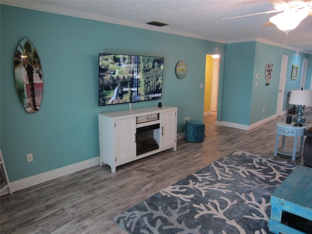 living room featuring ceiling fan, a textured ceiling, hardwood / wood-style floors, and ornamental molding