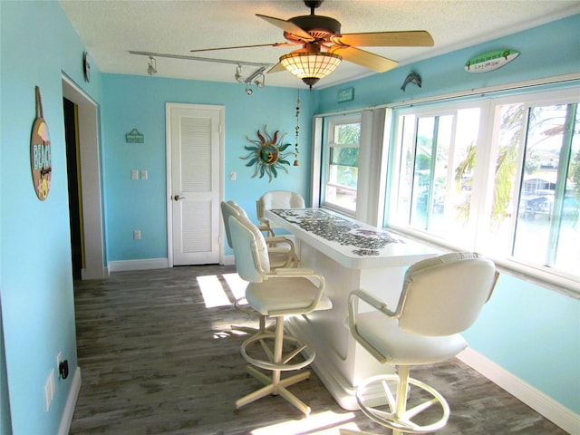 dining room with a textured ceiling, ceiling fan, dark wood-type flooring, and track lighting