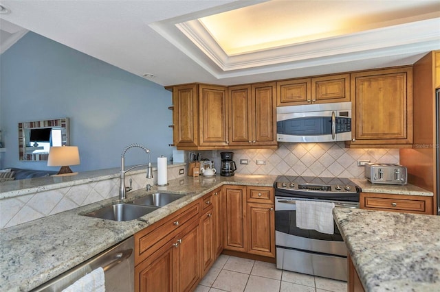 kitchen with light stone counters, stainless steel appliances, a tray ceiling, sink, and light tile patterned floors