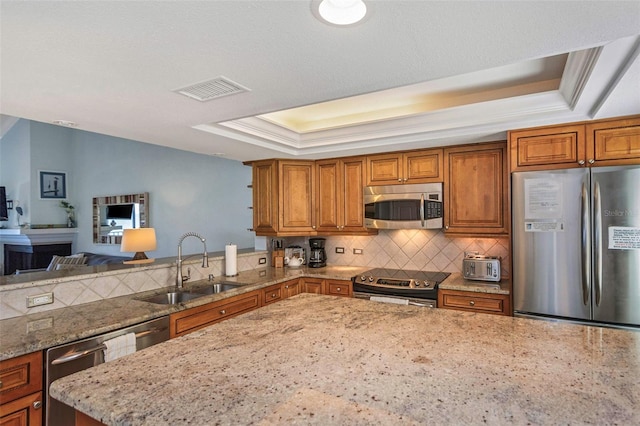 kitchen featuring crown molding, sink, light stone countertops, appliances with stainless steel finishes, and a tray ceiling