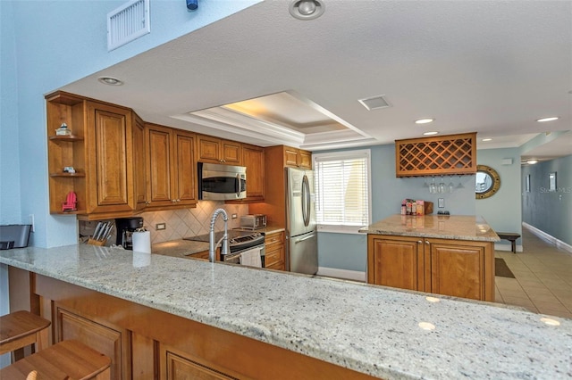 kitchen featuring stainless steel appliances, a kitchen breakfast bar, backsplash, kitchen peninsula, and a tray ceiling