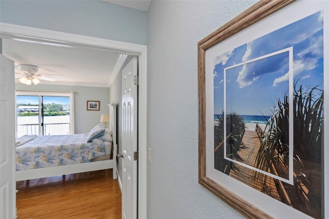 bedroom with hardwood / wood-style flooring, ceiling fan, ornamental molding, and a water view