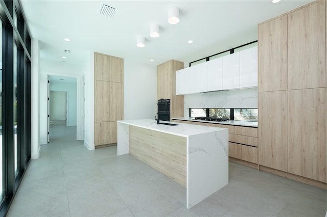 kitchen featuring light brown cabinetry, light stone counters, sink, a center island with sink, and black gas cooktop