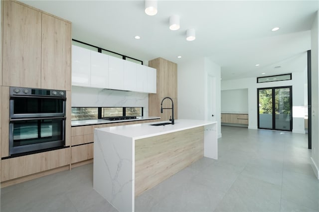 kitchen featuring light stone countertops, sink, stainless steel double oven, a kitchen island with sink, and white cabinets