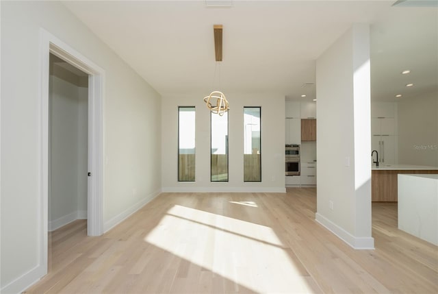 interior space with baseboards, light wood-style flooring, a notable chandelier, a sink, and recessed lighting