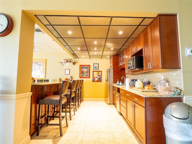 kitchen with light tile floors, a breakfast bar area, appliances with stainless steel finishes, backsplash, and light stone counters