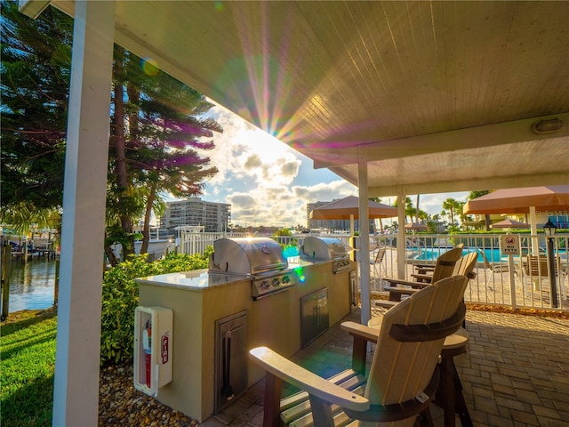 view of terrace with grilling area, an outdoor kitchen, a community pool, and a water view