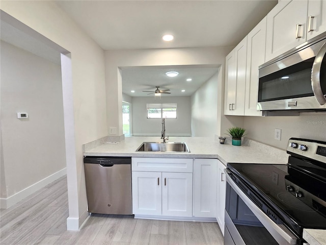 kitchen featuring appliances with stainless steel finishes, white cabinetry, sink, ceiling fan, and light hardwood / wood-style floors