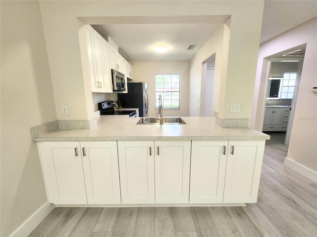 kitchen with white cabinetry, stainless steel appliances, sink, and light hardwood / wood-style flooring