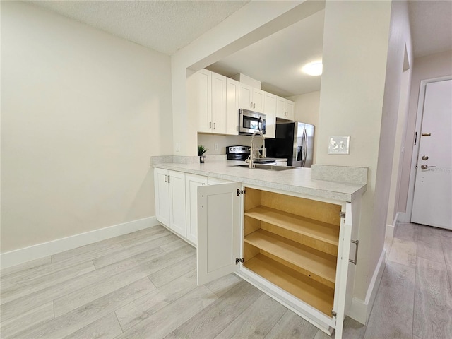 kitchen with stainless steel appliances, a textured ceiling, white cabinets, and light wood-type flooring