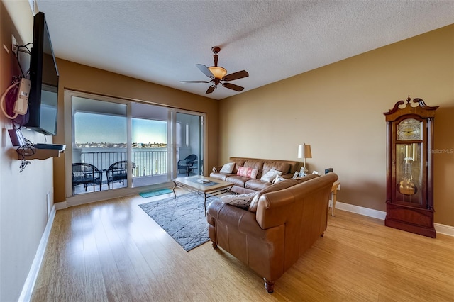 living room with a textured ceiling, ceiling fan, and light hardwood / wood-style flooring