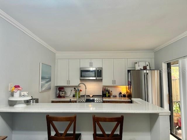 kitchen featuring white cabinets, a kitchen bar, a wealth of natural light, and stainless steel appliances