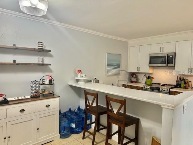 kitchen with crown molding, a kitchen breakfast bar, stainless steel appliances, and white cabinets