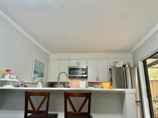 kitchen featuring crown molding, a kitchen breakfast bar, stainless steel appliances, and white cabinets